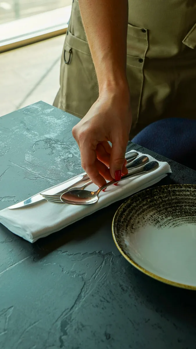 Main dressant les couverts sur une table en ardoise